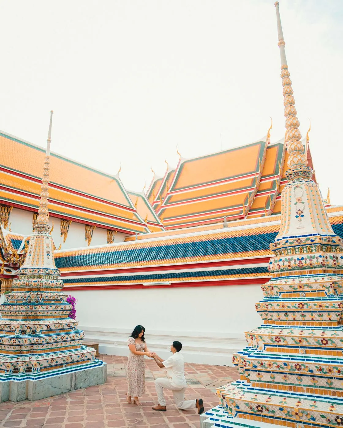 Couple at Wat Pho, with the temple roofline and tiled chedis behind them